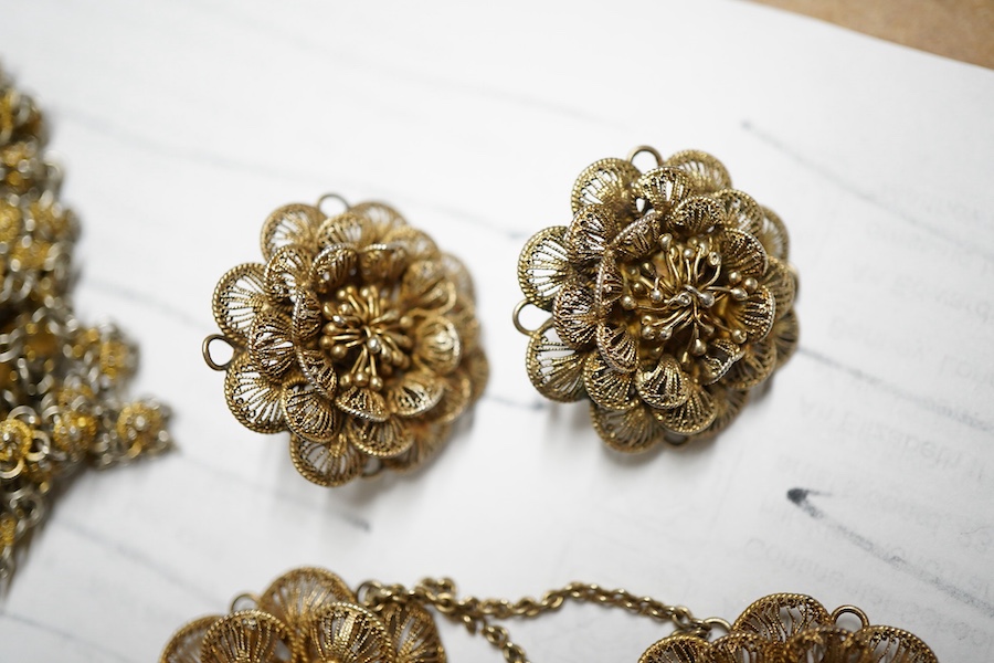 A gilt white metal filigree parure, comprising a necklace, 36cm, with flower head motifs, a pair of flower head earrings and a bracelet.